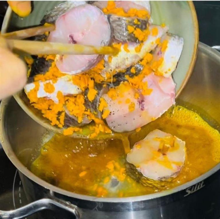 Bắt đầu kho cá lóc với nghệ bằng cách cho dầu ăn và bột nghệ vào đun nóng rồi đổ cá đã ướp vào. 